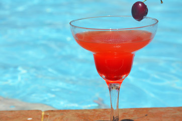 Tasty red cocktail background swimming pool. Margarita cocktail with a glass of cherries.