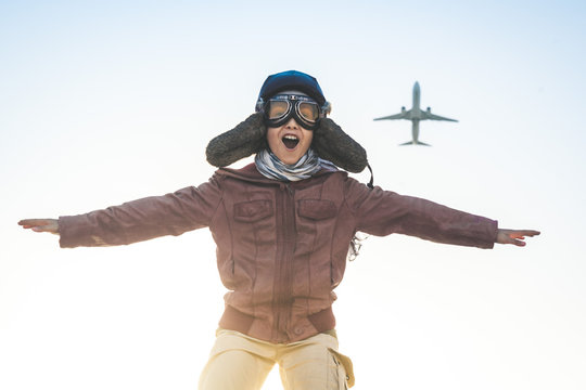 Handsome boy plays happily race with airplane joyfully pretending to take off disguised as a vintage aviation pilot hat, glasses mask leather jacket and fluttering foulard Concept image of kids dreams