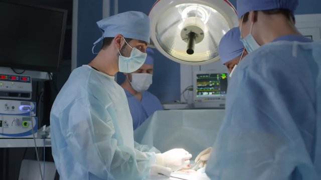Medium shot of two male doctors performing surgery while two assistants helping them in operating theater at hospital