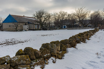 Winter landscape with peasant homestead surrounded with small stone wall in Skelky village,...