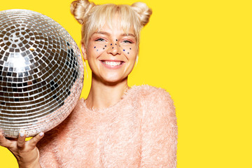 Portrait of cheerful caucasian model posing in studio with silver disco ball on yellow background....