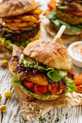 Vegan burger, carrot burger, homemade burger with carrot cutlet, grilled bell pepper, cherry tomatoes, red onion chutney, lettuce, and avocado sauce,on a white, wooden table. Healthy eating concept