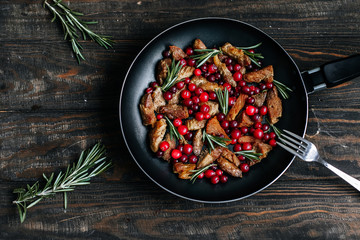 Roast pork with cranberries, olives and rosemary in a pan on a dark wooden table top view