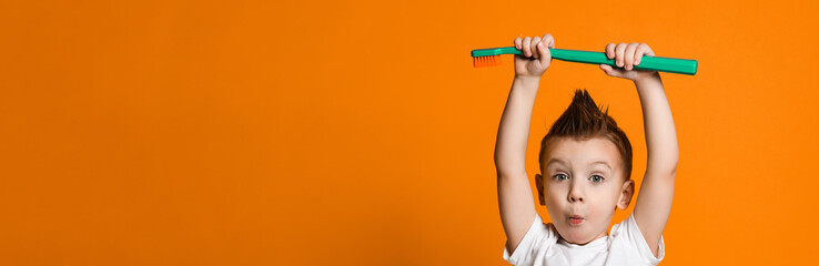 Portrait of a little boy holding a tooth brush over yellow background