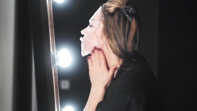 Beauty Teenage Girl applying cosmetic face mask and admiring herself in the mirror.