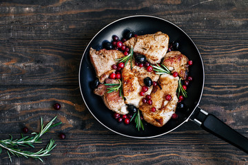 Roast pork with cranberries, olives, rosemary and red onion in a pan on a dark wooden table top view