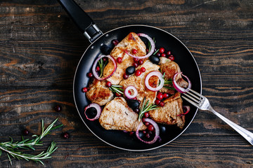 Roast pork with cranberries, olives, rosemary and red onion in a pan on a dark wooden table top view