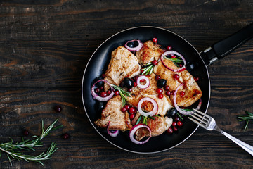 Roast pork with cranberries, olives, rosemary and red onion in a pan on a dark wooden table top view