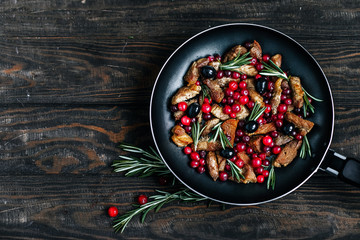 Roast pork with cranberries, olives and rosemary in a pan on a dark wooden table top view