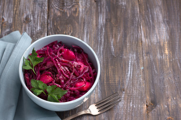 Stewed red cabbage with apples, spices and greens on a wooden background, free space. delicious homemade healthy food