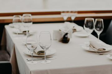 Decorated served table with cutlery and glasses for wedding reception or other festive event. Round table with cutlery, white tableclothes. Empty plates for food