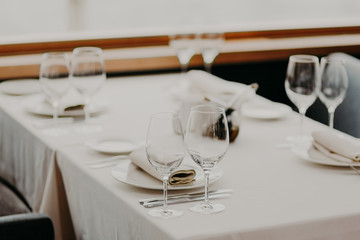 Horizontal view of festive decorated table with empty wineglasses and plates against blurred background. Cutlery on festive table. Wedding decoration concept