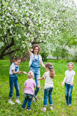Obraz premium Woman and four little girls playing in blooming apple blossom garden.
