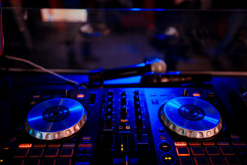Obraz premium DJ with headphones at night club party under the blue light and people crowd in background