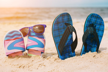 Two pairs of flip-flops in sand on beach. Sunglasses on one of them. Summer vacation concept. Sea...