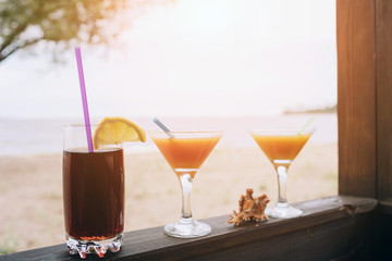 Summer concept: fresh exotic cocktails on wooden edge. Shell lying between glasses. Cola with straw and lemon. Island life. Paradise.
