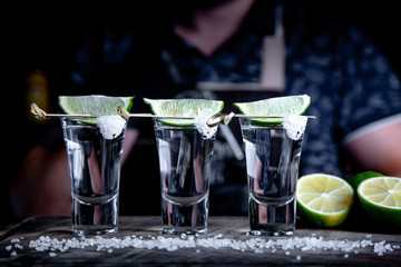 aperitif with friends in the bar, three glasses of alcohol with lime and salt for decoration. Tequila shots, selective focus
