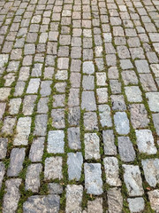 Old street of rectangular granite stones in perspective, with weeds at the joints.