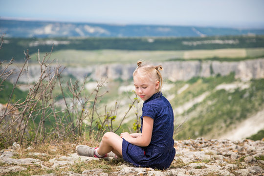 Blonde girl in the blue dress sitting jn the rock