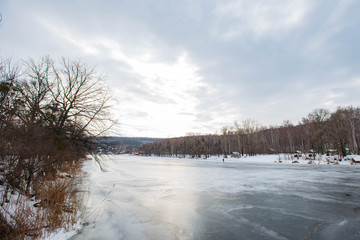 A view of the frozen river in the snow-covered forest on a cloudy winter day,