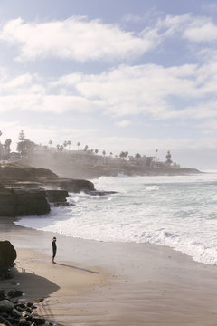 Man standing on the beach at the coast of the Pacific Ocean in San Diego. The waves cause a mist of sea water.