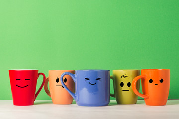 A lot of multicolored cups with funny faces on a green background. The concept of a friendly...