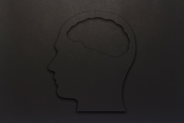 Black cardboard head with a brain on a black background. Copy space. Flat lay, top view.