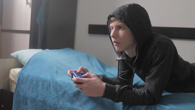 young teen and joystick man cybersport hooded sweater absorbed In online video game. boy teenager in the hood playing video lifestyle games on the console on the gamepad. Controller console gamepad
