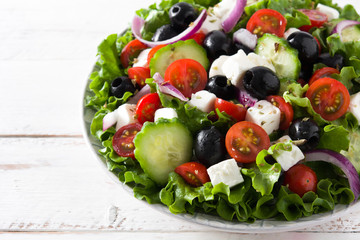 Fresh Greek salad in bowl with black olive,tomato,feta cheese, cucumber and onion on white wooden table.
