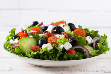 Fresh Greek salad in bowl with black olive,tomato,feta cheese, cucumber and onion on white wooden table.