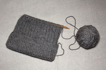 process of knitting men's hats with an elastic band with a lapel and a round crown of gray acrylic, a warm stylish winter hat