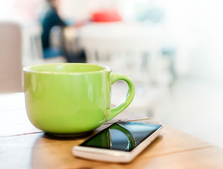 A big green mug with a drink and a smartphone on a wooden table in a cafe - 244930819