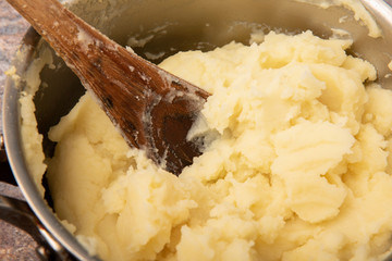 Close up image of a pan of mashed potato with a wooden spoon 