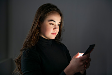 A young teenager girl using mobile phone in dark room