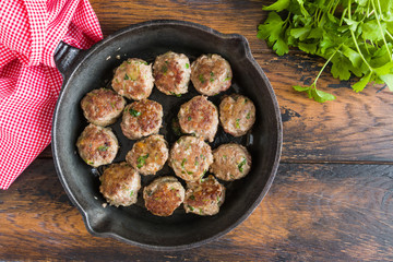 Fried meatballs in black pan on wooden rustic table, top view