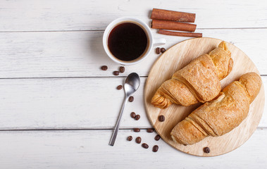 two croissants with cup of coffee on wooden kitchen board on white wooden background