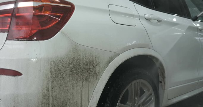 Professional guy (man) in a car wash washes a very dirty car using Karcher and splashes foam, wipes the car with a sponge. Concept of: Car wash, Wash accessories, Under high pressure.
