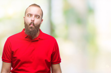 Young caucasian hipster man wearing red shirt over isolated background making fish face with lips, crazy and comical gesture. Funny expression.