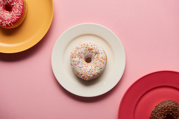 top view of sweet delicious donuts on plates on pink background