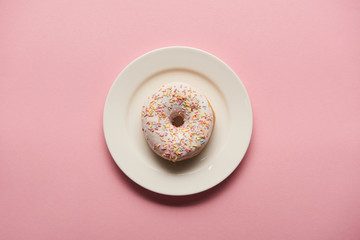 top view of delicious donut on white plate on pink background
