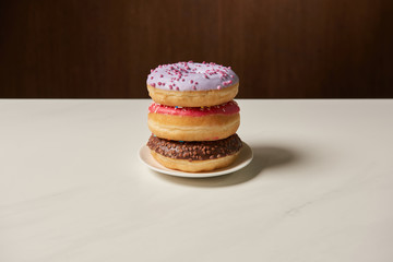 tasty donuts with icing and sprinkles on plate on white table