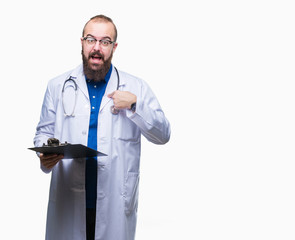 Young doctor man holding clipboard over isolated background with surprise face pointing finger to himself