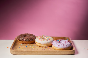 tasty glazed donuts sprinkles on wooden cutting board on pink background