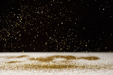 selective focus of bright sparkles falling on white table isolated on black