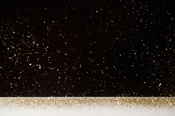 selective focus of golden sparkles falling on white table isolated on black