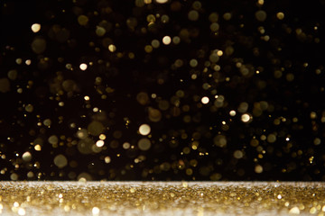 selective focus of bright sparkles falling on table isolated on black