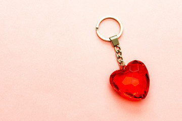 Keychain with red heart made of transparent cut glass or faceted stone on a soft pink paper...