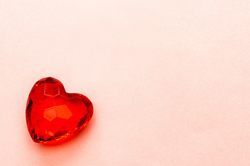 Red heart made of transparent cut glass or faceted stone on a soft pink paper background, copy space