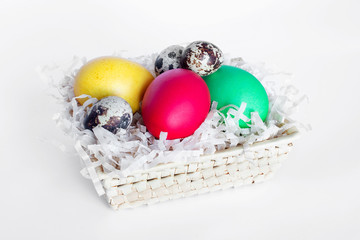 Multi-colored Easter eggs lie in a basket on a white background. Yellow, red, green and quail eggs i