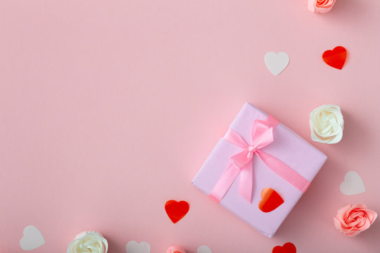background of gifts with confetti hearts and roses, boxes wrapped in decorative paper on pastel colored pink background, top view, holiday concept and love